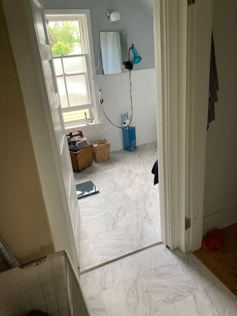Bathroom with white marble floor, window light, and a small mirror above a cabinet.